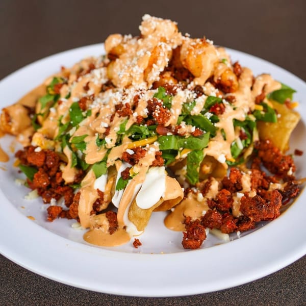 A plate of loaded nachos with chorizo, shrimp, lettuce, cheese, and a creamy sauce.