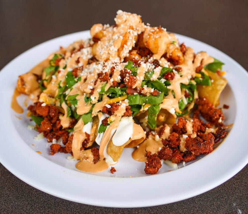 A plate of loaded nachos with chorizo, shrimp, lettuce, cheese, and a creamy sauce.