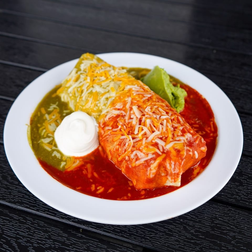 A smothered burrito with red and green sauce, topped with cheese, sour cream, and guacamole.