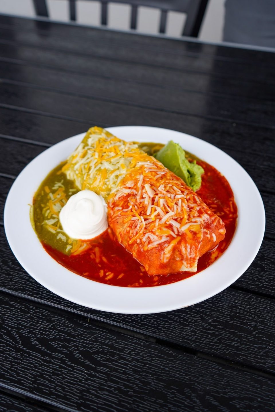 A smothered burrito with red and green sauce, topped with cheese, sour cream, and guacamole.