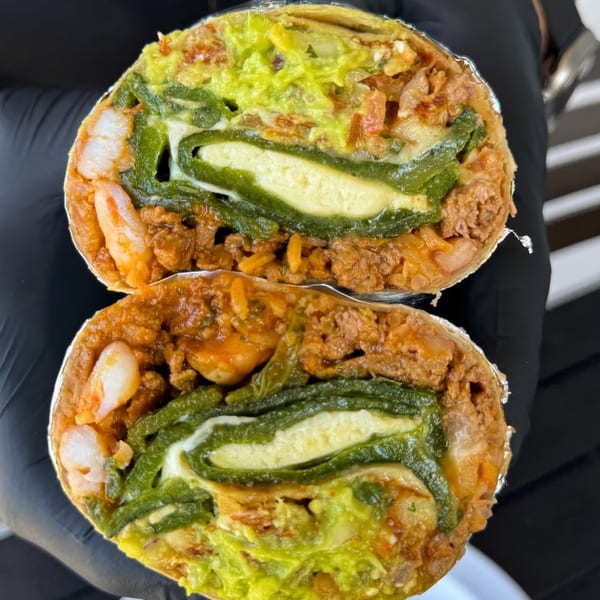 Two halves of a burrito revealing shrimp, meat, rice, guacamole, and a chile relleno.