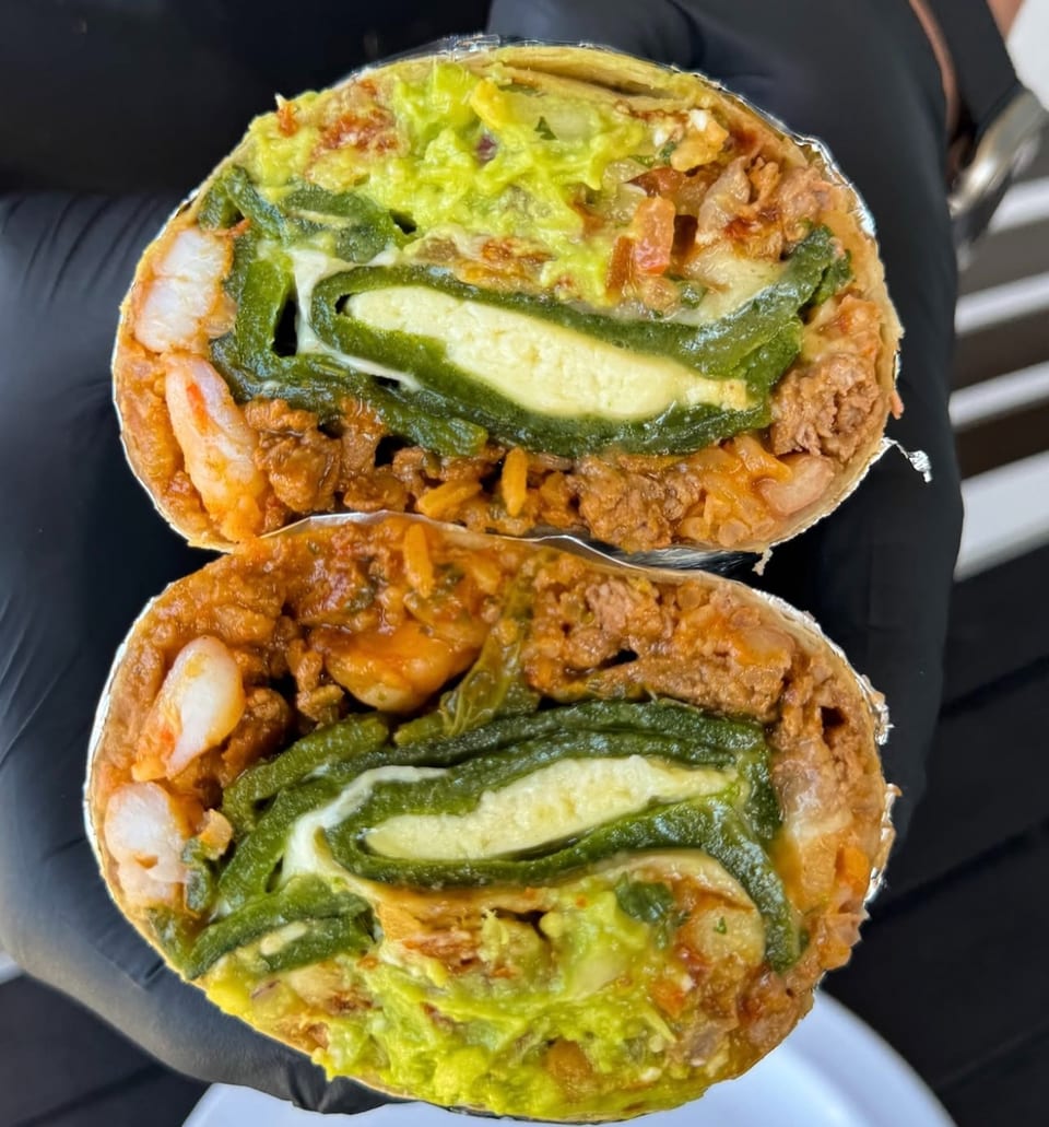 Two halves of a burrito revealing shrimp, meat, rice, guacamole, and a chile relleno.