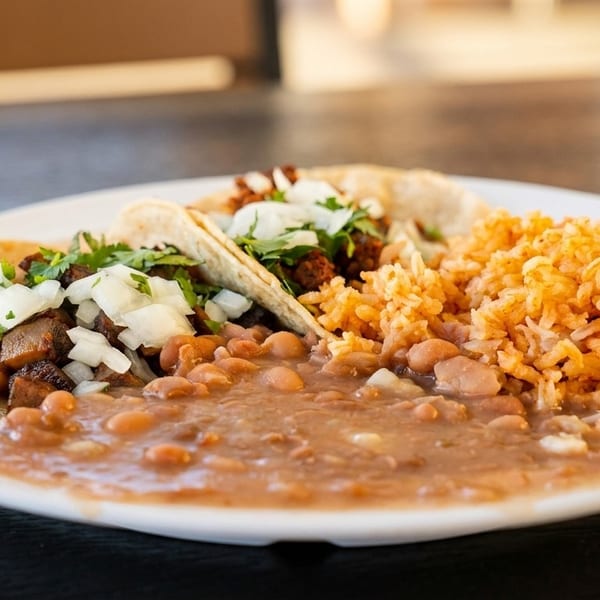 Two tacos with meat, onions, and cilantro, served with pinto beans and Spanish rice.