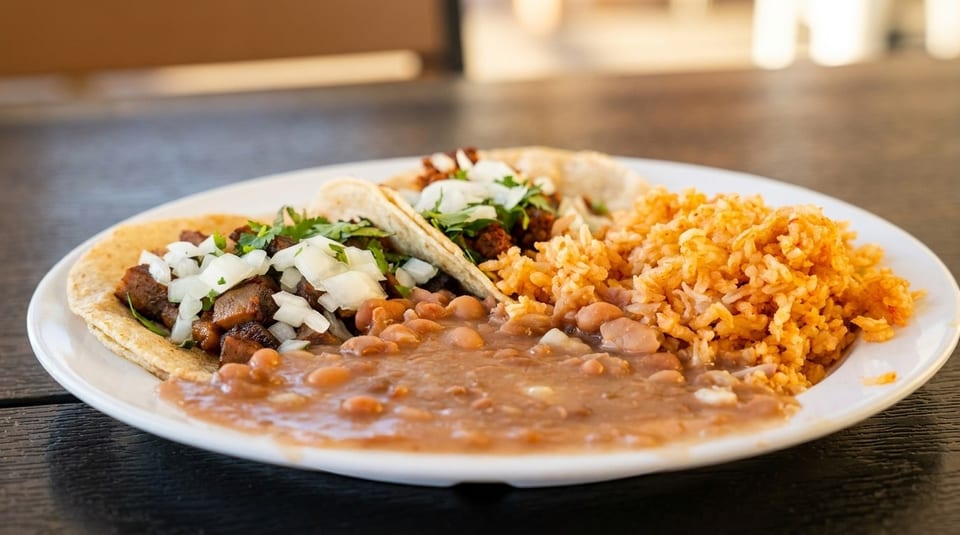 Two tacos with meat, onions, and cilantro, served with pinto beans and Spanish rice.